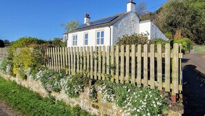 Une maison blanche avec une clôture en bois et des plantes en fleurs devant.