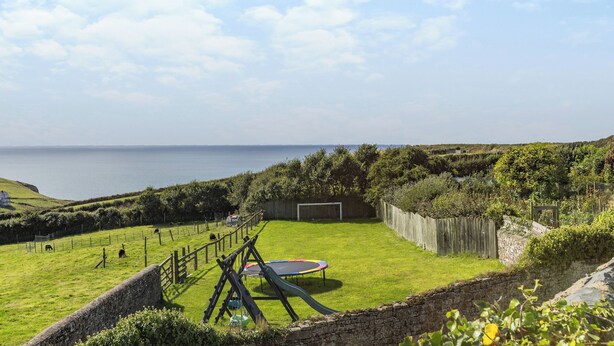 A grassy outdoor area with a trampoline, a wooden fence, and a view of the sea.