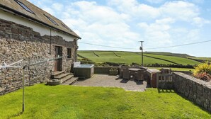 A stone building with a patio area, outdoor seating, and a view of rolling hills.