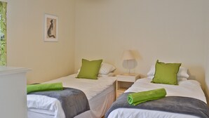 Une chambre avec deux lits simples, chacun agrémenté d’un oreiller vert et d’une serviette verte roulée. Une table de chevet avec une lampe se trouve entre les deux lits.