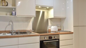 A modern kitchen with white cabinetry, a stainless steel range hood, a built-in oven, and a wooden countertop.