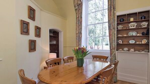 A dining room with a wooden table and chairs, a vase of flowers, and a window with curtains. - The Old Butler's House (Cley-next-the-Sea)