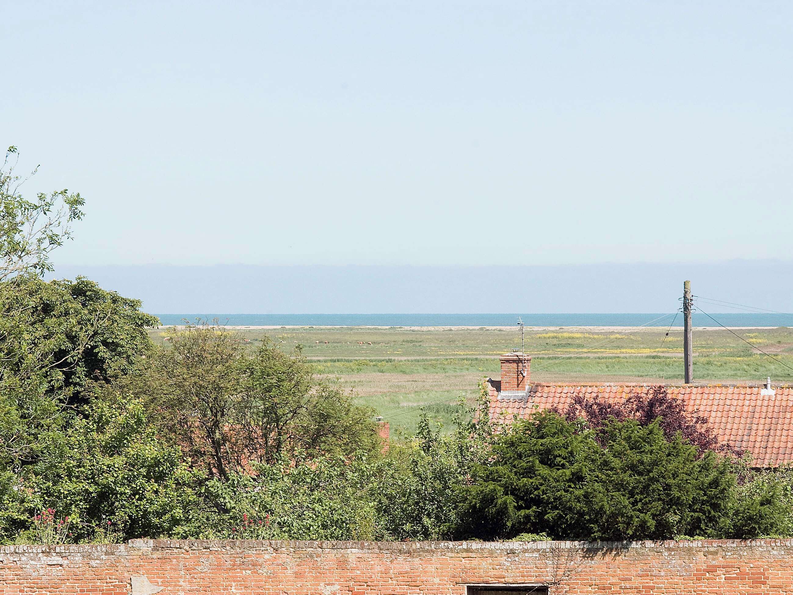 Un paysage rural offrant une vue dégagée sur la mer, avec un mur de briques et quelques arbres.