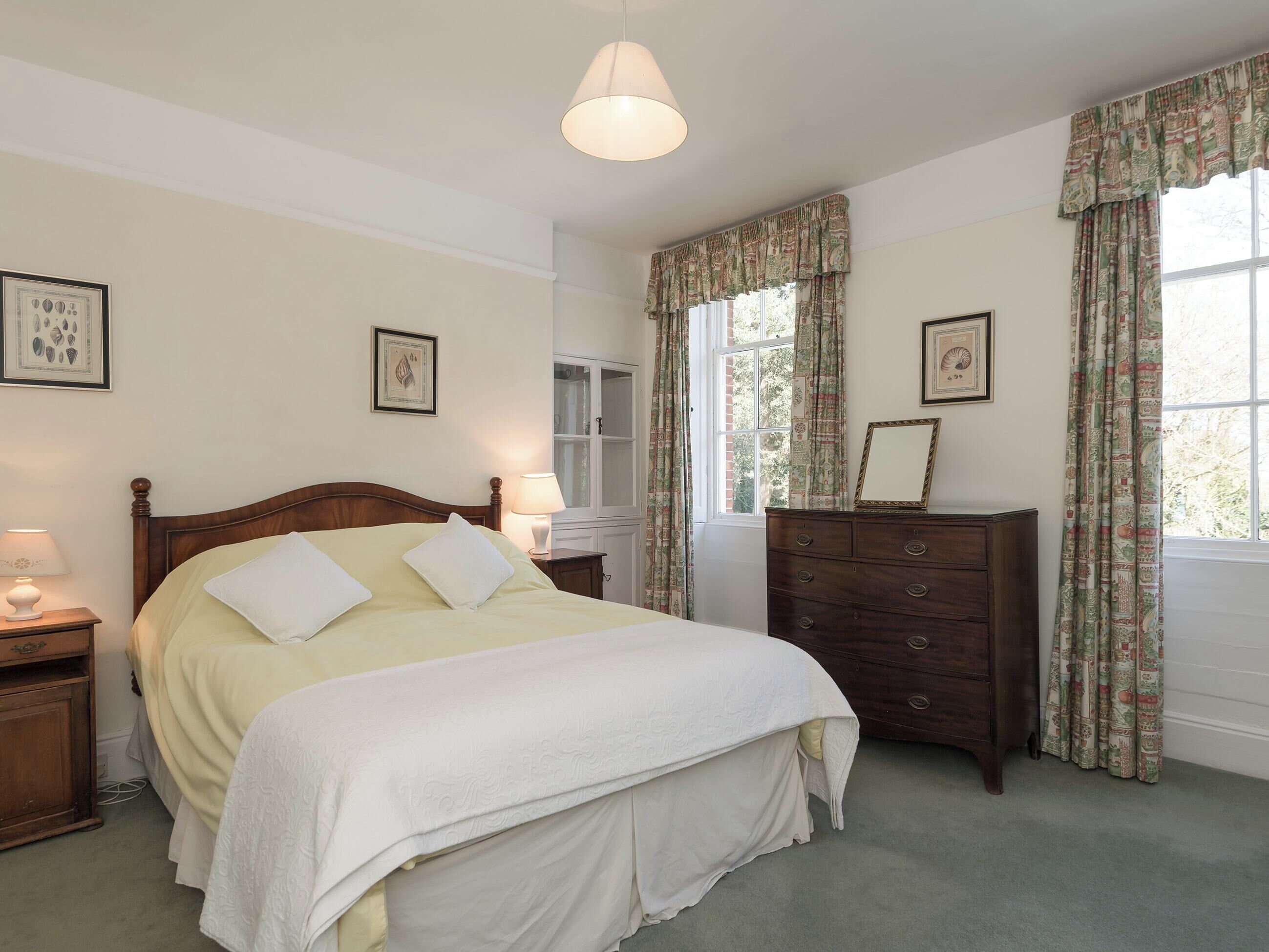 A bedroom with a wooden bed, two bedside tables with lamps, a dresser, and a window with curtains.