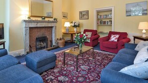 A living room with a fireplace, red armchairs, blue sofas, a coffee table, and a bookshelf. - The Old Butler's House (Cley-next-the-Sea)