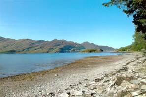 A rocky shoreline with a calm lake and mountains in the background.