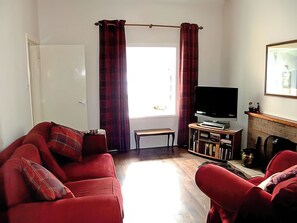 A living room with a red sofa, a television, a bookshelf, and a fireplace. - 2 bedroom accommodation in Arnisdale, near Glenelg (Arnisdale, near Glenelg)