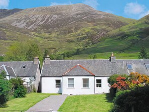 A white cottage with a red roof, a stone chimney, and a small front garden.