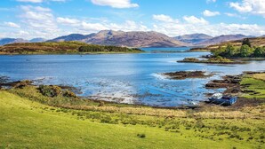 A scenic view of a lake with mountains in the background, a grassy foreground, and a small boat docked near the shore. - 2 bedroom accommodation in Arnisdale, near Glenelg (Arnisdale, near Glenelg)