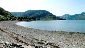 Une plage de galets bordée d’un lac paisible, avec des montagnes en arrière-plan.