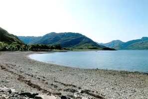 A pebbly beach with a calm lake and mountains in the background.