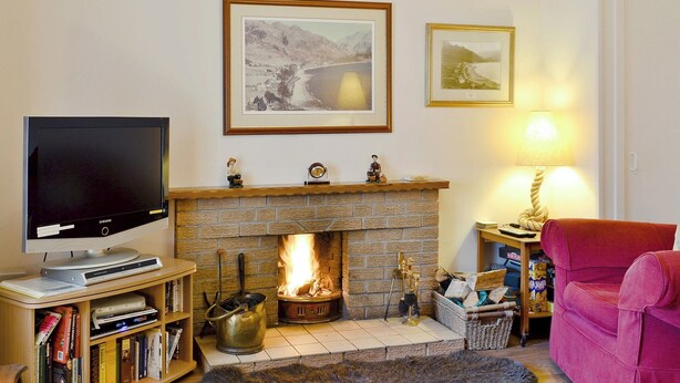 A living room with a fireplace, a television, and framed pictures on the wall. - 2 bedroom accommodation in Arnisdale, near Glenelg (Arnisdale, near Glenelg)