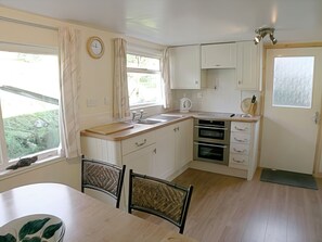 A kitchen with a dining table, chairs, a clock, cabinets, and a window with curtains.