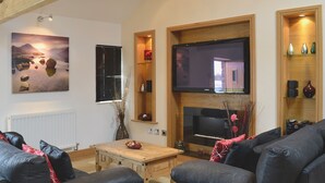 A living room with a fireplace, a flat-screen TV, and a large painting. - 2 bedroom accommodation in Tynlon, near Rhosneigr (Tynlon, near Rhosneigr)