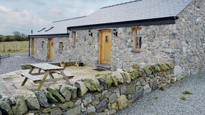 A stone building with a sloped roof, wooden doors, and a stone wall surrounding the patio area. - 2 bedroom accommodation in Tynlon, near Rhosneigr (Tynlon, near Rhosneigr)