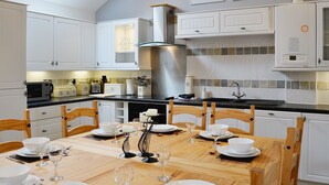 A modern kitchen with white cabinetry, a dining table set for six, and a large stove. - 2 bedroom accommodation in Tynlon, near Rhosneigr (Tynlon, near Rhosneigr)