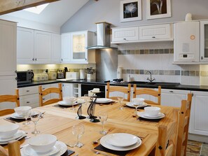 A modern kitchen with white cabinetry, a dining table set for six, and a large stove. - 2 bedroom accommodation in Tynlon, near Rhosneigr (Tynlon, near Rhosneigr)