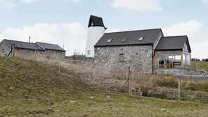 A stone building with a white tower, a wooden structure with a glass enclosure, and a stone wall with a fence. - 2 bedroom accommodation in Tynlon, near Rhosneigr (Tynlon, near Rhosneigr)