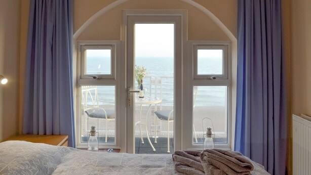 A bedroom with a large bed, a view of the sea through a glass door, and a balcony with chairs and a table. - 1 bedroom accommodation in Pevensey Bay (Pevensey Bay)