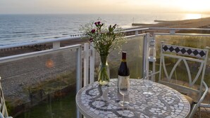 A balcony with a view of the sea, a table with a bottle and a glass, and a vase with flowers. - 1 bedroom accommodation in Pevensey Bay (Pevensey Bay)