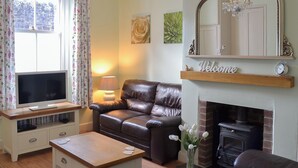 A cozy living room with a leather sofa, a TV on a wooden stand, a fireplace, and a 'Welcome' sign above it. - 2 bedroom accommodation in Buckfastleigh (Buckfastleigh)