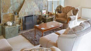 A living room with a stone fireplace, a comfortable armchair, a sofa, and a coffee table. - 3 bedroom accommodation in Constantine, near Falmouth (Constantine, near Falmouth)