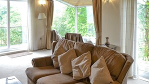 A spacious living room with a large window, a sofa with multiple cushions, a wooden coffee table, and a lamp. - 3 bedroom accommodation in Constantine, near Falmouth (Constantine, near Falmouth)