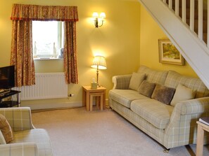A living room with a sofa, a small table with a lamp, a radiator, a television, and a staircase.