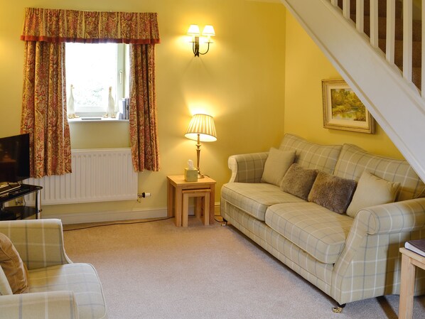 A living room with a sofa, a small table with a lamp, a radiator, a television, and a staircase.