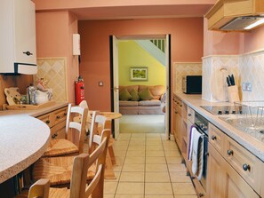 A kitchen with wooden cabinets, a dining area with chairs, a sofa, and a staircase leading to another room.