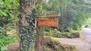 A sign reading "SNARESBROOK" attached to a tree in a wooded area.