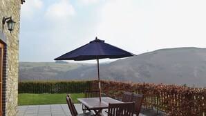 Une terrasse avec une table et des chaises, un parasol et une vue sur les collines.