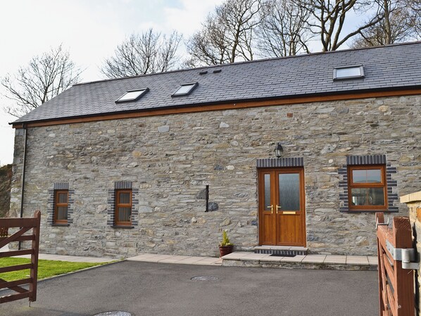 A stone building with a sloped roof, two windows, a wooden door, and a small porch area.