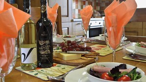 Une table dressée avec une bouteille de vin, un verre de vin, un saladier rempli de salade, une assiette de fromage et des crackers.