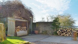 A rustic outdoor area with a wooden shed, a gravel path, and stacks of firewood. - 2 bedroom accommodation in Pentrich, near Ripley (Pentrich, near Ripley)
