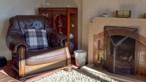 A leather armchair with a plaid pillow, a wooden cabinet, and a fireplace with a metal screen. - 2 bedroom accommodation in Pentrich, near Ripley (Pentrich, near Ripley)