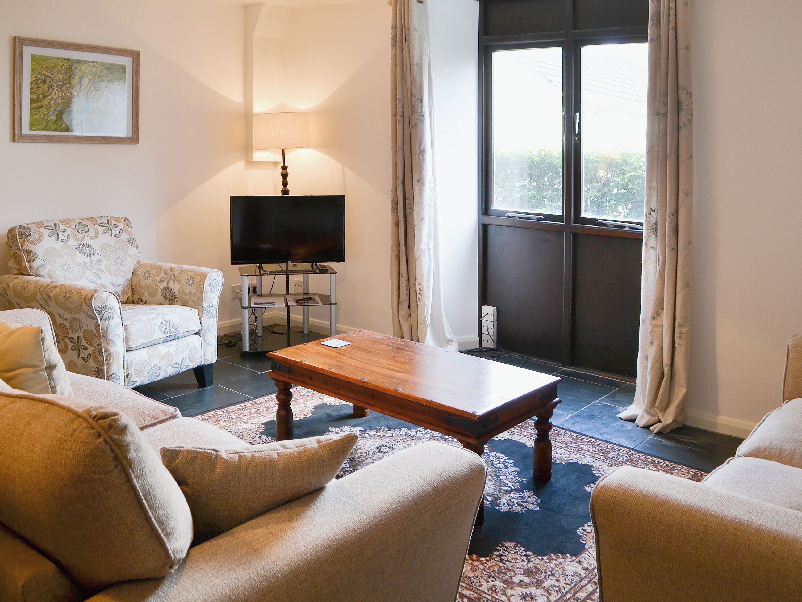 A living room with a sofa set, a coffee table, a TV on a stand, and a window with curtains.