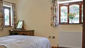 Un dormitorio con una cama, una mesita de noche de madera, una ventana con cortinas florales y un radiador.