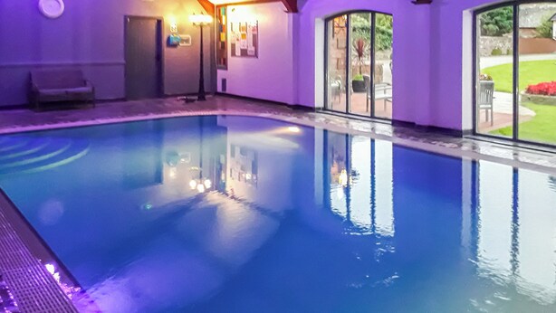An indoor swimming pool with clear water, wooden beams on the ceiling, and a view of the outdoors through large windows. - 1 bedroom accommodation in Arkleby, near Cockermouth (Arkleby, near Cockermouth)