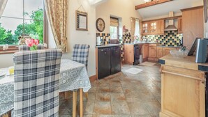 A cozy kitchen with a dining area, featuring a checkered tablecloth, wooden cabinets, and a view of greenery outside. - 1 bedroom accommodation in Arkleby, near Cockermouth (Arkleby, near Cockermouth)