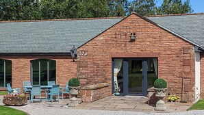 A brick building with a tiled roof, a patio with blue chairs, and potted plants. - 1 bedroom accommodation in Arkleby, near Cockermouth (Arkleby, near Cockermouth)