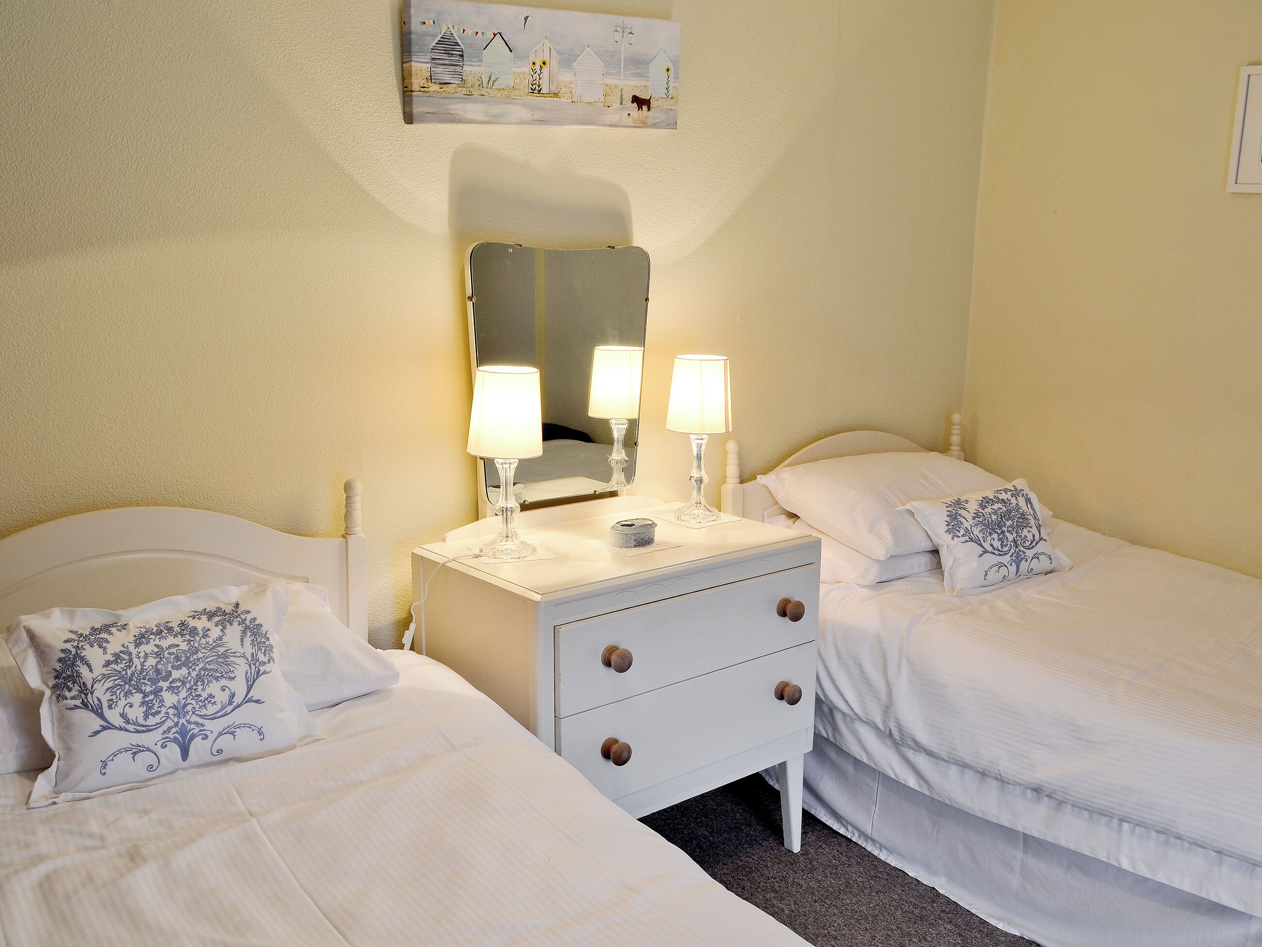 Une chambre d’hôtel avec deux lits, une table de chevet avec des lampes, un miroir et une œuvre d’art accrochée au mur.