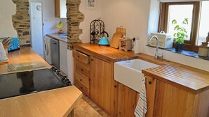 Una cocina con armarios de madera, un arco de piedra, un hervidor azul y una ventana con plantas.
