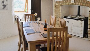 Un comedor con una mesa de madera dispuesta para cuatro, una botella de vino y un reloj sobre una chimenea de piedra.