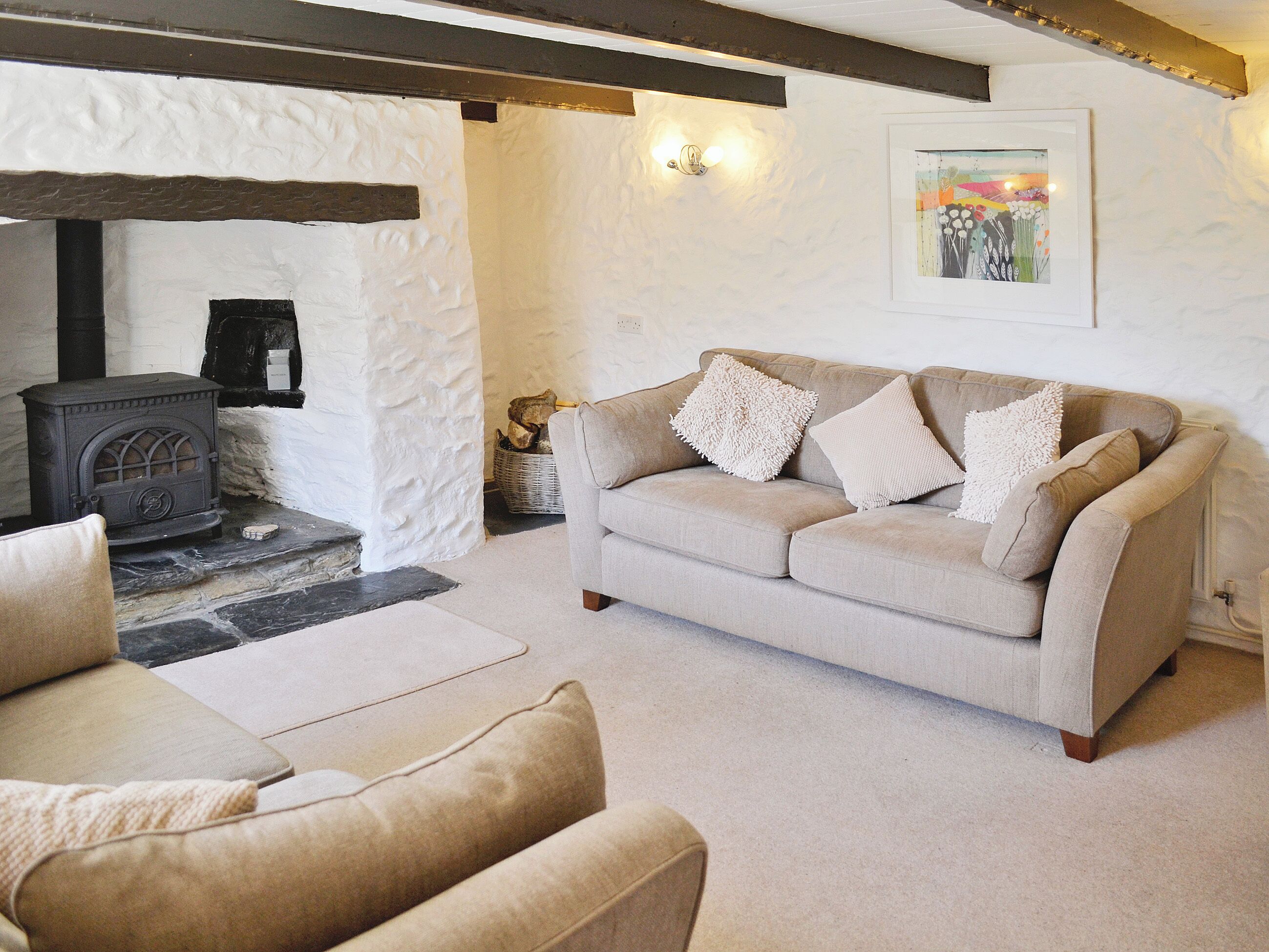 A cozy living room with a beige sofa, two armchairs, a fireplace, and a framed artwork on the wall.