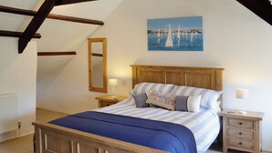 Un dormitorio con una cama de madera, una mesita de noche, una lámpara de noche, un espejo y un cuadro con barcos a vela en la pared.