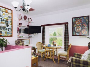 Ein Wohnzimmer mit Fernseher, Korbstühlen, einem Tisch und einem Bücherregal.