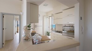 A modern kitchen with white cabinetry, a built-in oven, and a large island with a vase and jar of items. - L'Attico di Alessia by Perle di Puglia (Maruggio)