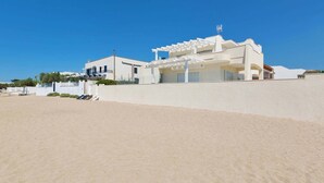 A modern white building with a covered outdoor area and a sandy beach in the foreground. - L'Attico di Alessia by Perle di Puglia (Maruggio)