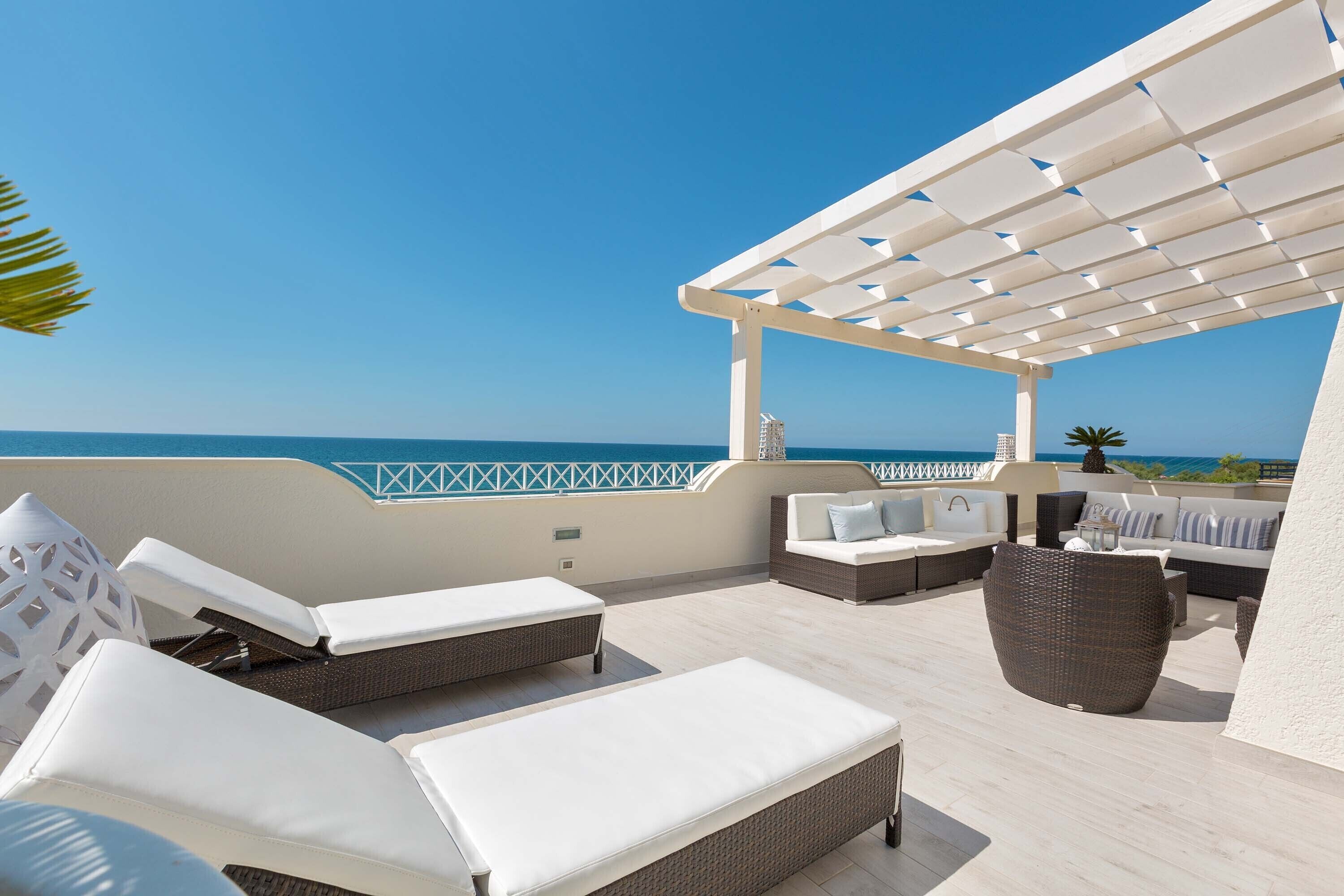 A rooftop terrace with lounge chairs, a sofa, and a pergola overlooking the sea.
